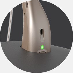 La imagen muestra una toma de cerca con el audífono en el cargador