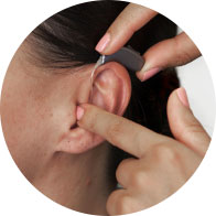Image shows person placing hearing aid inside woman's ear