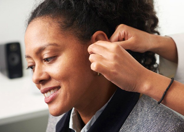 Image shows hand placing hearing aids into woman's ear