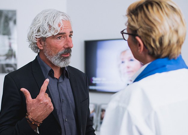 La imagen muestra un hombre hablando con un audioprotesista en un centro auditivo