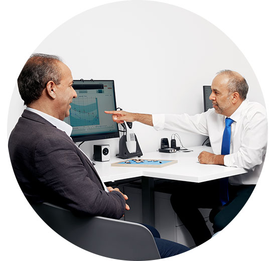 L’image montre un homme qui parle à un audioprothésiste devant un écran qui présente un audiogramme