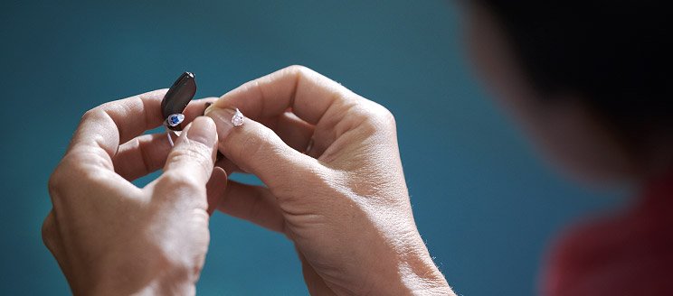 Image shows hands exchanging hearing aid batteries