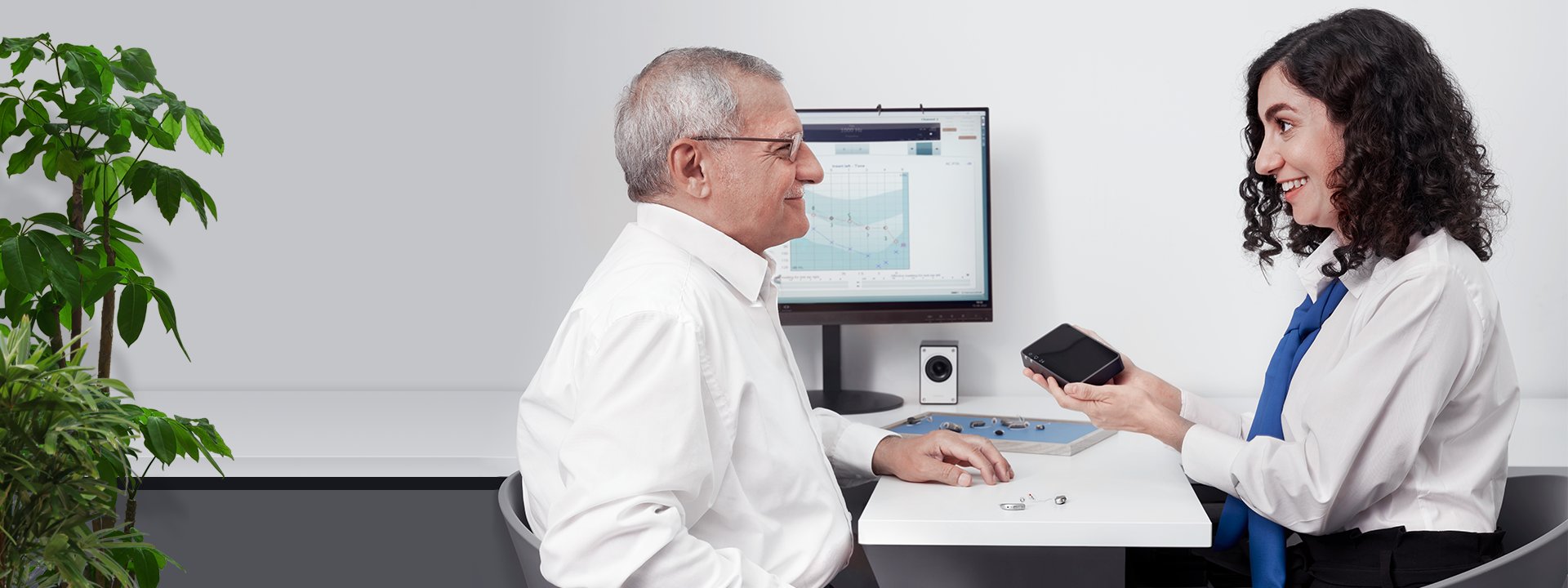 Image d’un homme qui parle à un audioprothésiste dans un centre auditif devant un écran avec un audiogramme