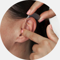 L’image montre une main qui place un appareil auditif dans l’oreille