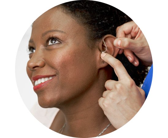 L’image montre une femme à qui l’on place un appareil auditif derrière l’oreille